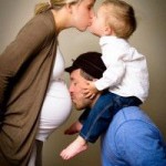 Une maman enceinte qui fait un bisou à son aîné qui est sur les épaules de son papa